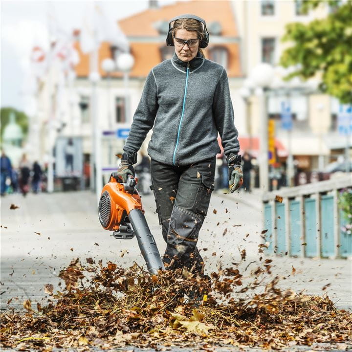 Woman with a hand-held leaf blower on a city street